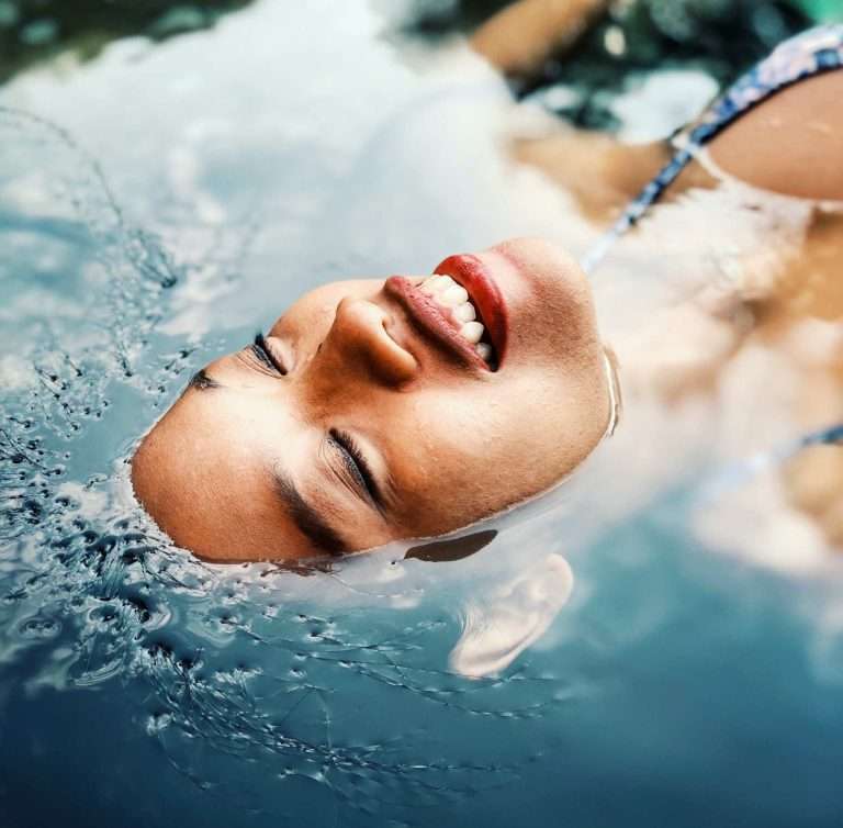 Viso di giovane donna che emerge dall'acqua. L'acqua micellare è una fonte di benessere per la pelle del viso