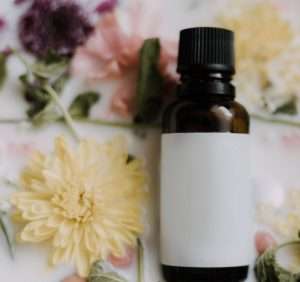 Immagine di boccetta di vetro scuro di olio di calendula e sullo sfondo neutro fiori gialli e rosa