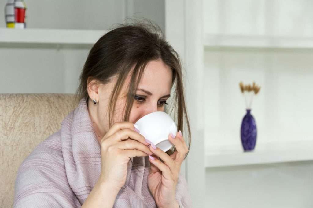 Donna in veste da camera affetta da raffreddore primaverile che sorseggia una tisana
