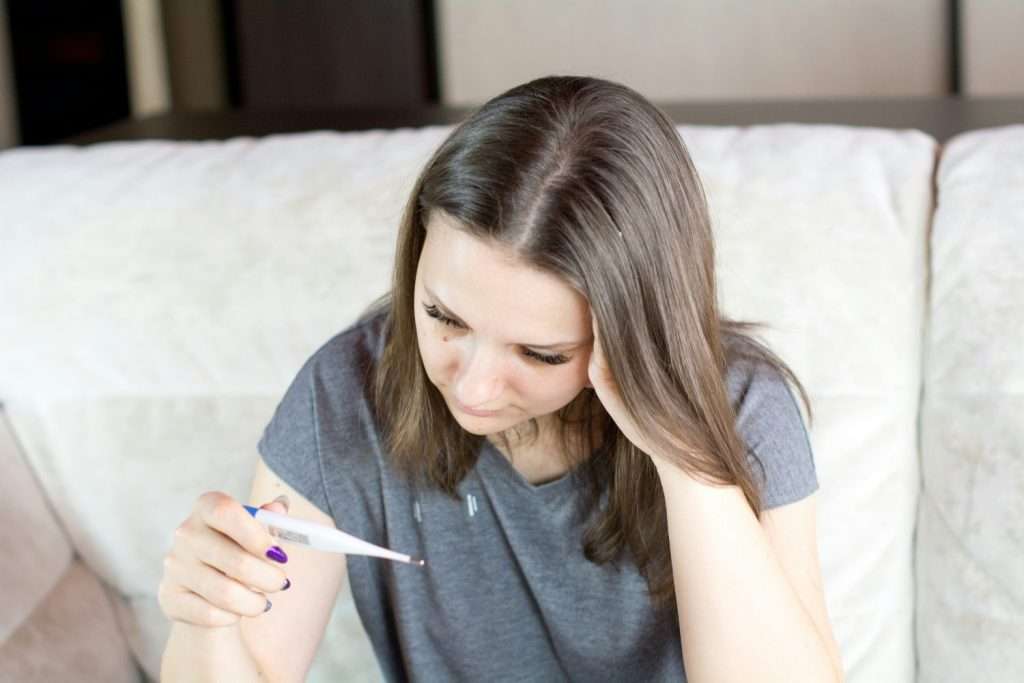 Giovane donna che misura la febbre forse affetta da raffreddore primaverile o sindrome parainfluenzale
