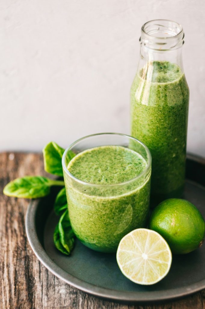 per avere una pelle radiosa sfrutta i centrifugati come quello nel grande bicchiere di vetro trasparente su un piatto grigio con un ciuffo di basilico e mezzo lime