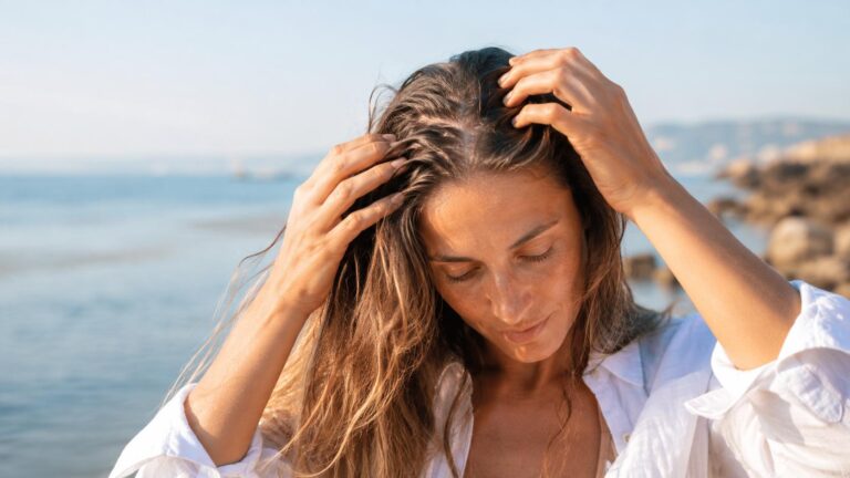 Donna al mare che tocca la cute, immagine per articolo su secchezza del cuoio capelluto durante l’estate